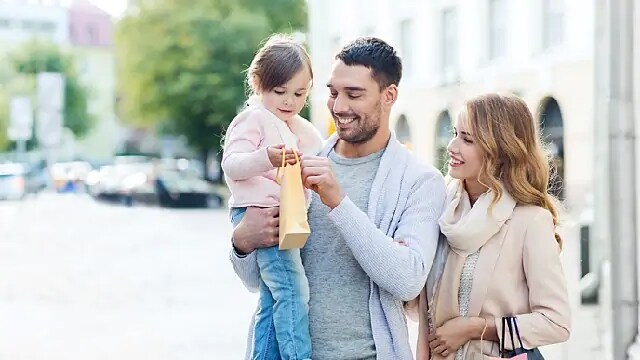 A man holds a child while a smiling woman looks on