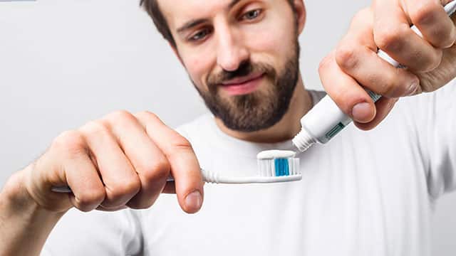 A man putting some tooth paste on a tooth brush