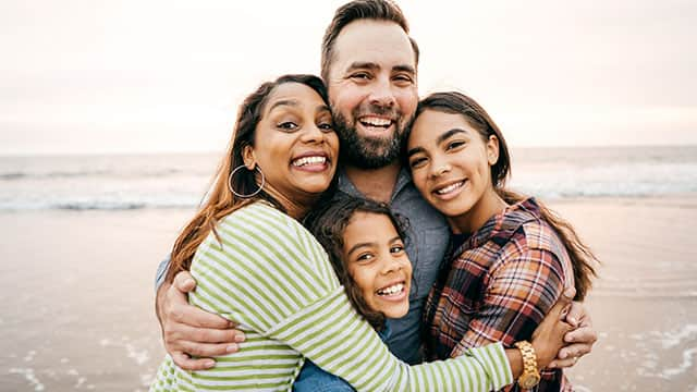 Mother and Father in big hug with daughters on ocean beach