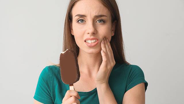 Young woman is feeling tooth ache while eating ice cream