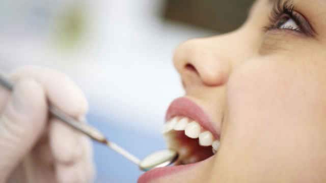 a close up of a woman teeth inspected with dental mirror